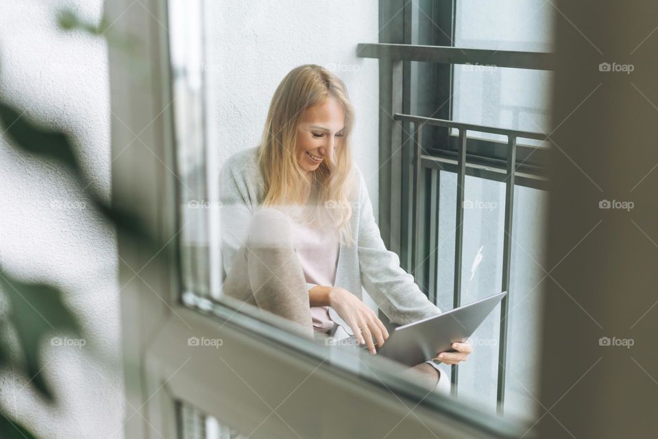 Beautiful blonde young woman freelancer in home wear using laptop on the balcony