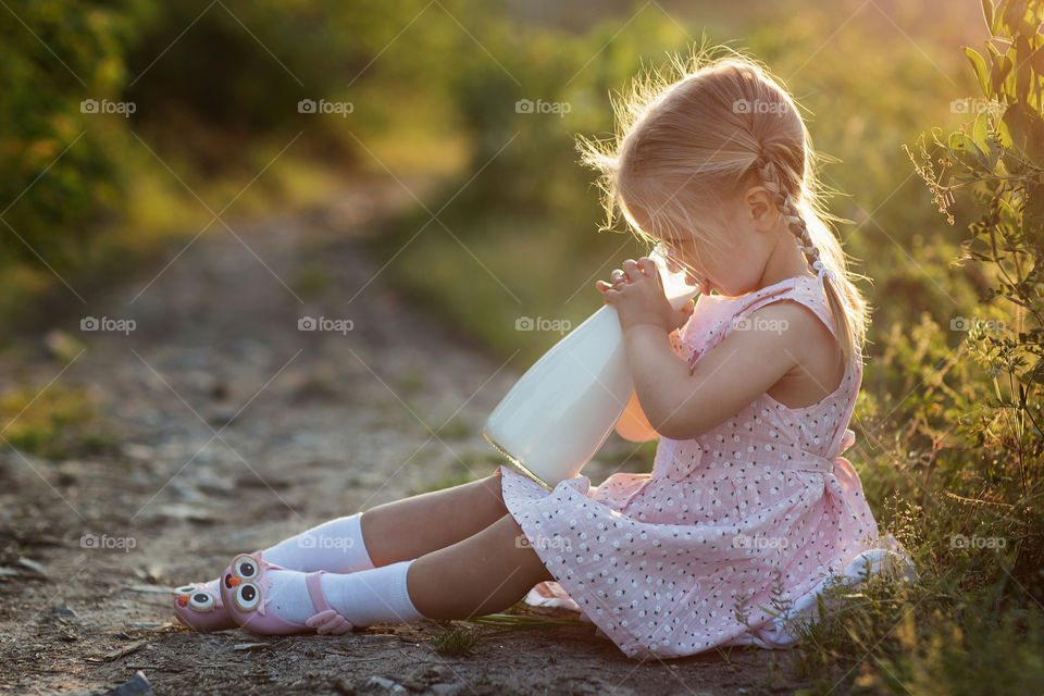 Little girl with blonde hair drinking milk outdoor 
