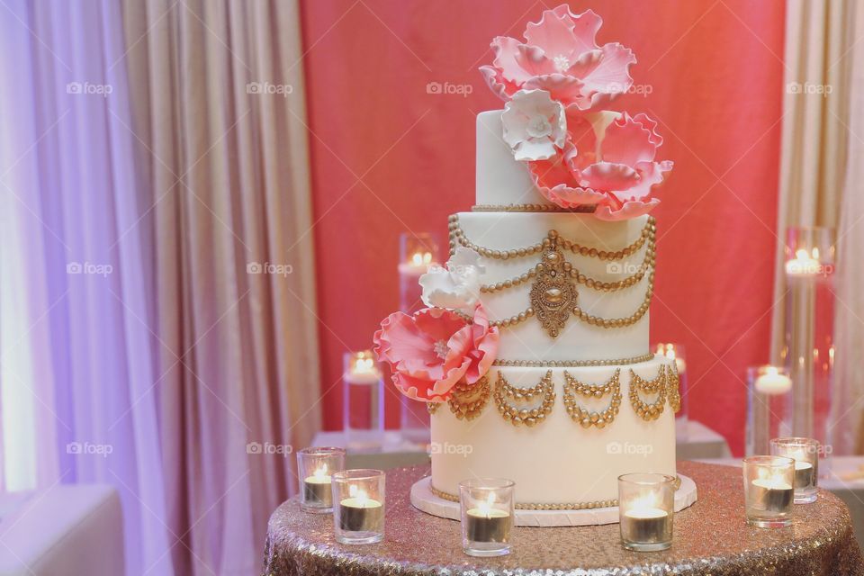 A fancy cake with massive pink flowers and decorated in gold