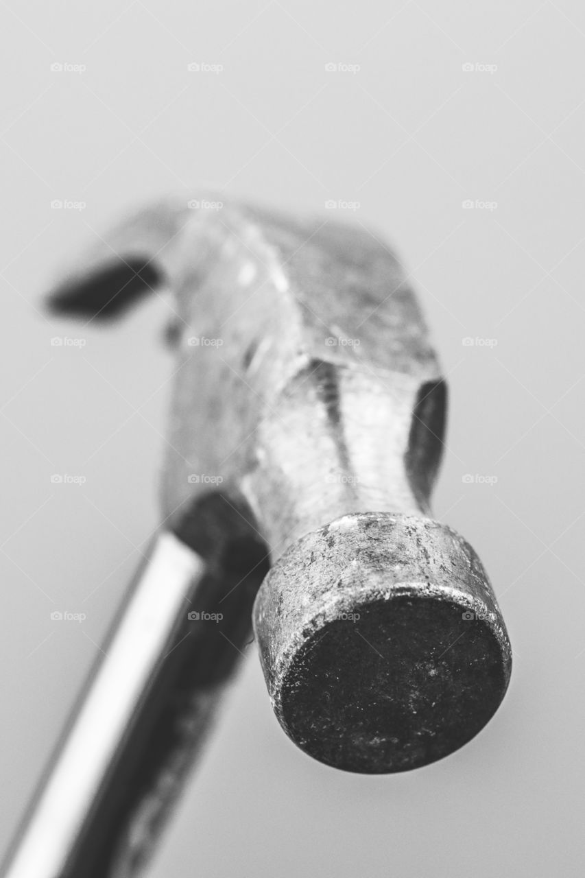 A black and white close up portrait of a metal claw hammer. it looks like the viewer is the nail.