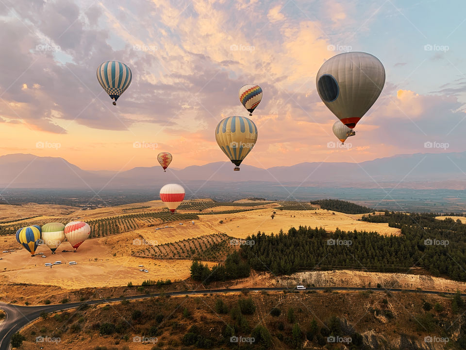 Hot air balloons flying over the beautiful landscape with open road and tiny white car on it