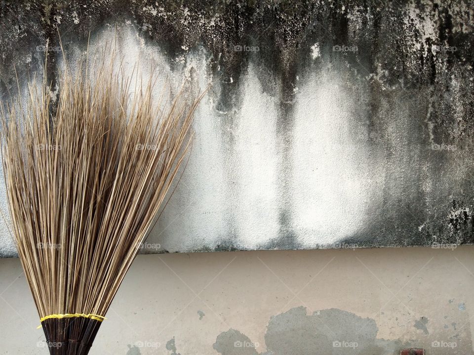 The stick broom or  tagmaprgaw broom is leaning against the stained white concrete wall.