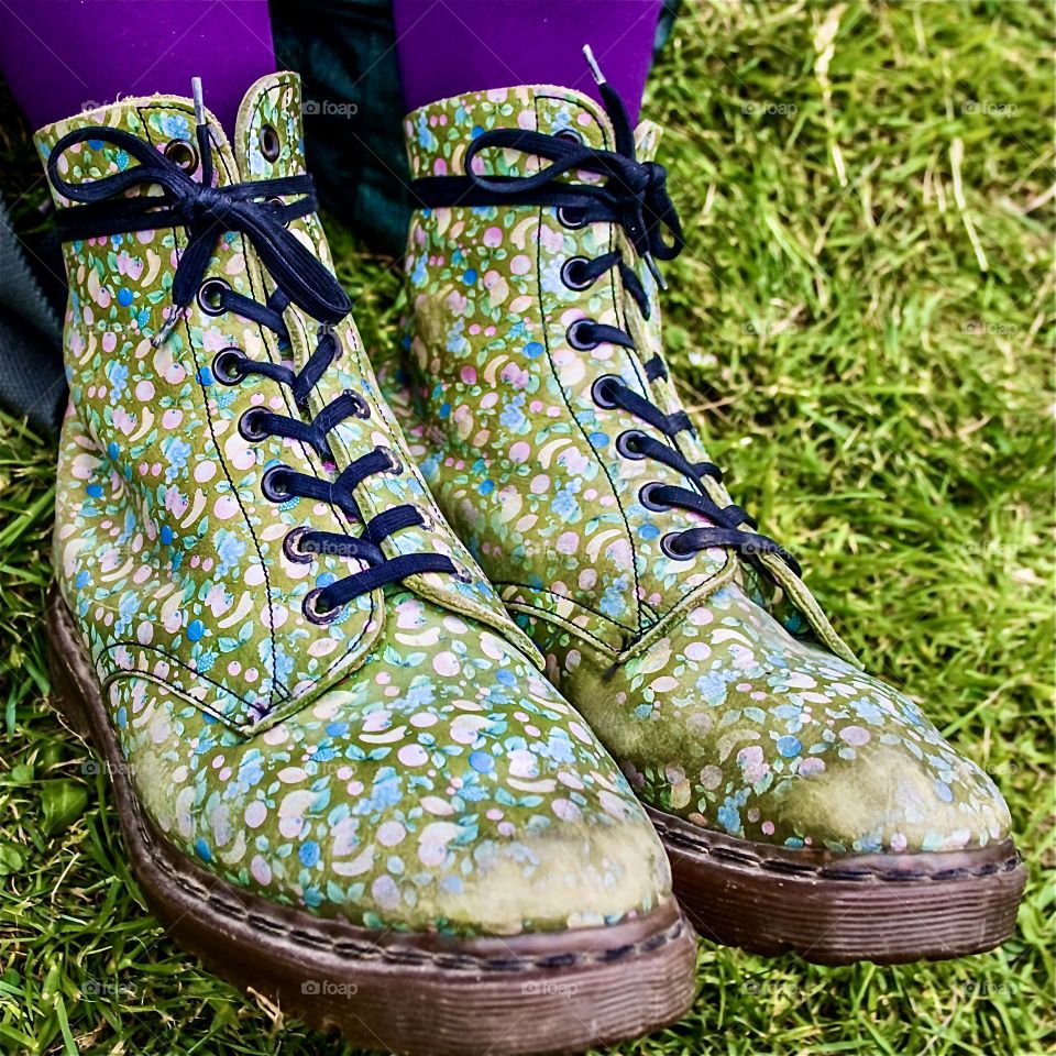 Old green DMs with a faded fruit pattern on them, worn with purple tights against a grassy background 