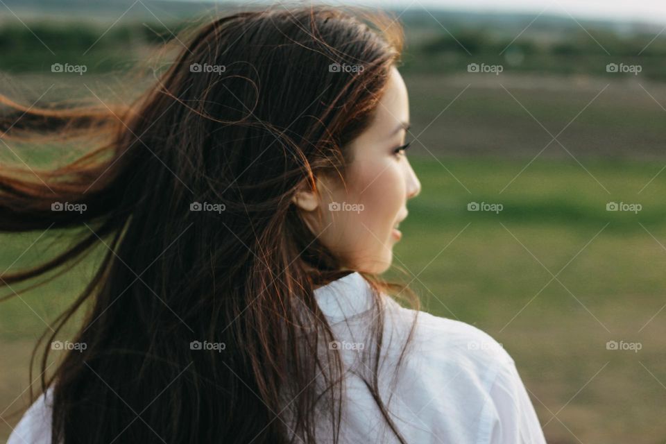 Close up portrait of beautiful long hair girl in white clothes in field, view from back. Sensitivity to nature concept