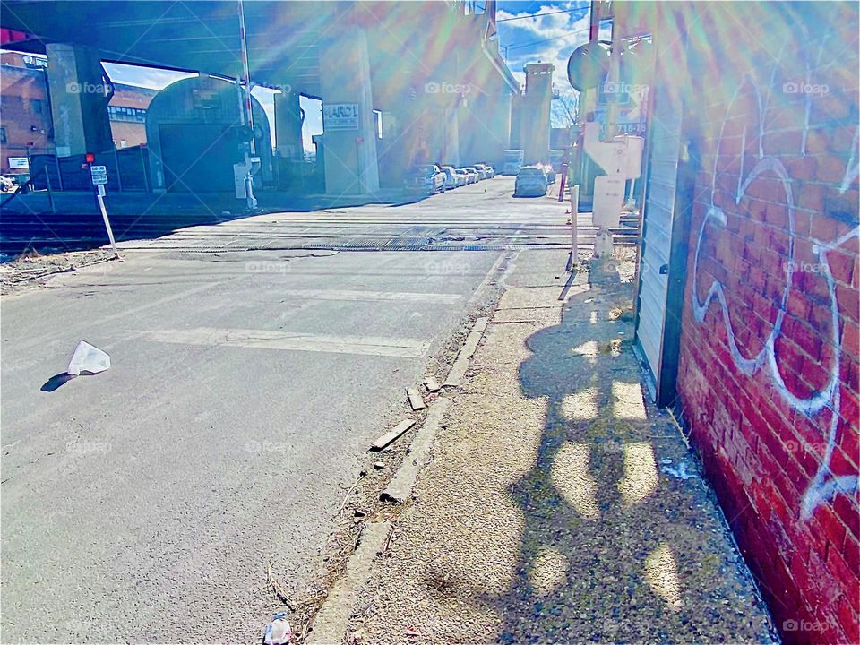 The sun creates strong refraction & lens flare effects at certain times at the parking lot under the Pulaski Bridge in LIC, Queens. The “NO CROSSING” sign in front of the train tracks cast a large beautiful shadow as well. 2022. Hypnotic Productions