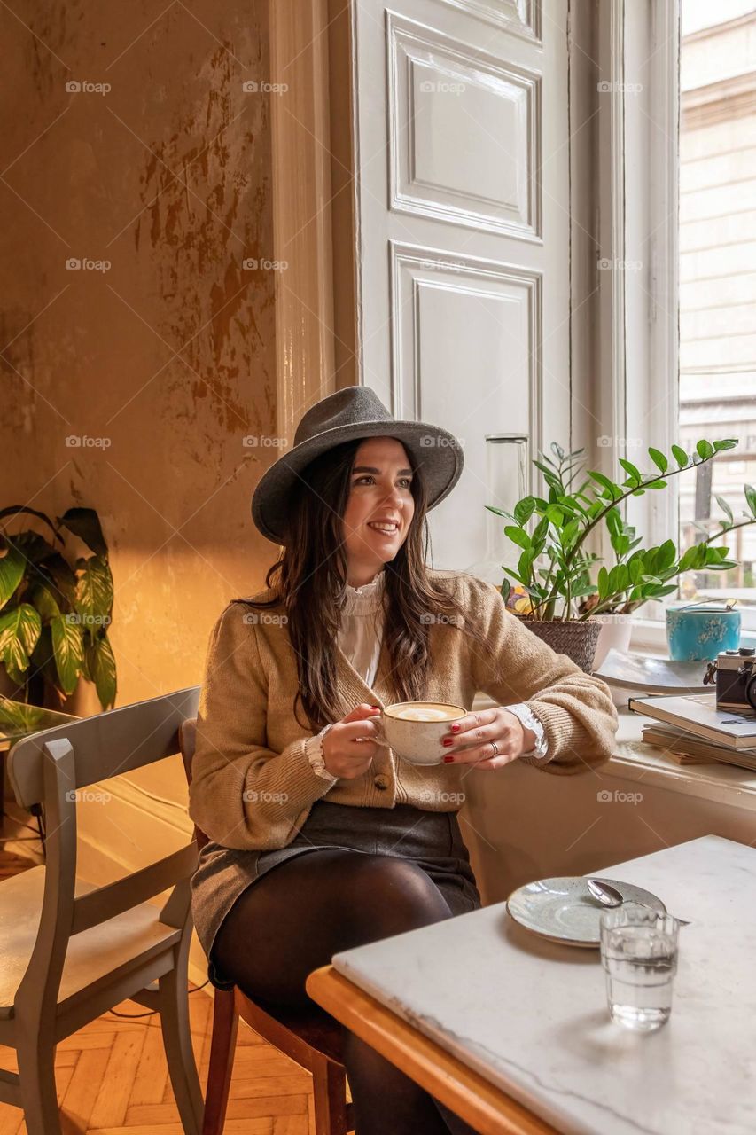 Young woman sitting by the window while drinking in stylish cafe