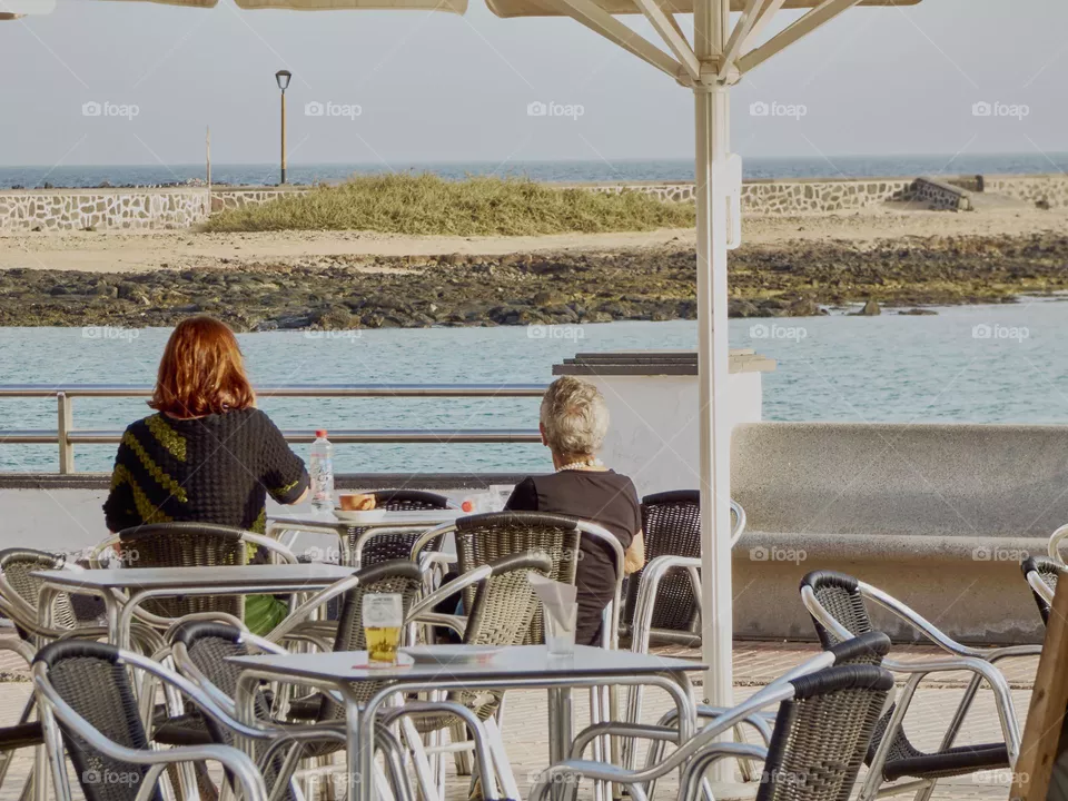 pareja de mujeres sentadas en un bar tomando algo con vistas al mar a la luz de el atardecer