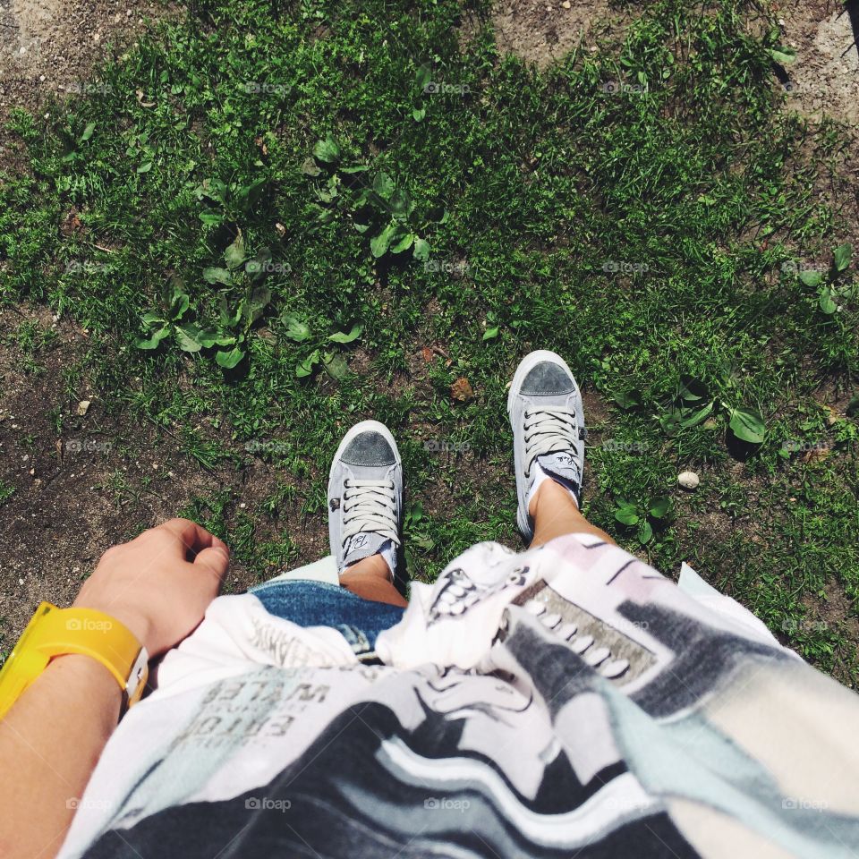 Girl in a t-shirt, denim shorts and grey sneakers with yellow plastic watches standing on a green summer meadow with sunny clear weather