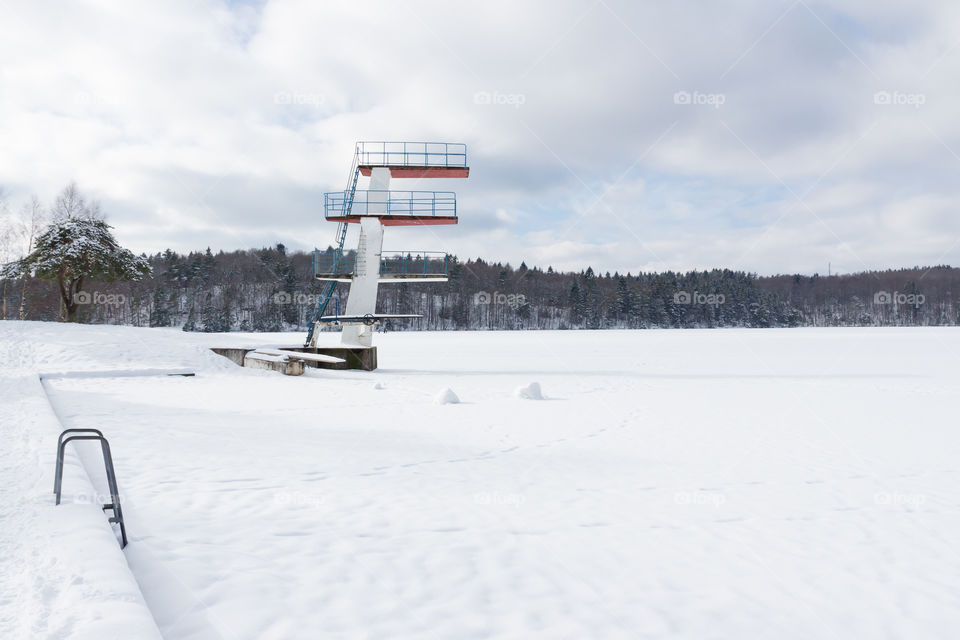 Snow covered swimming area and diving tower in frozen lake, winter 