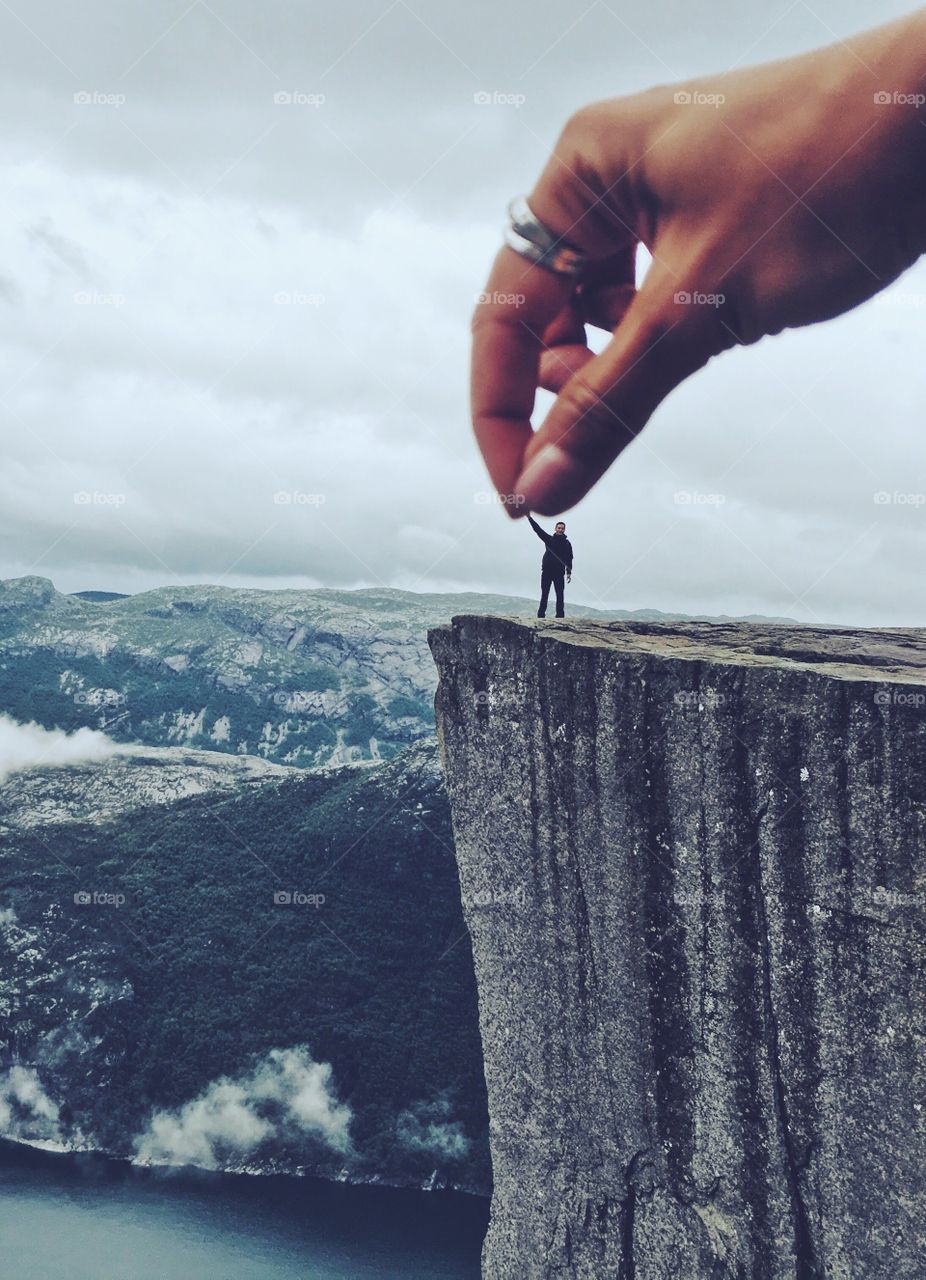 Big hand from the sky holding a tiny silhouette standing on the edge of Prekestolen rock.