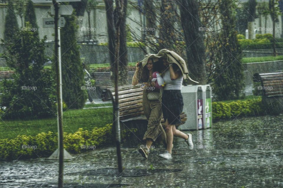 two girls run in the rain covered with one jacket