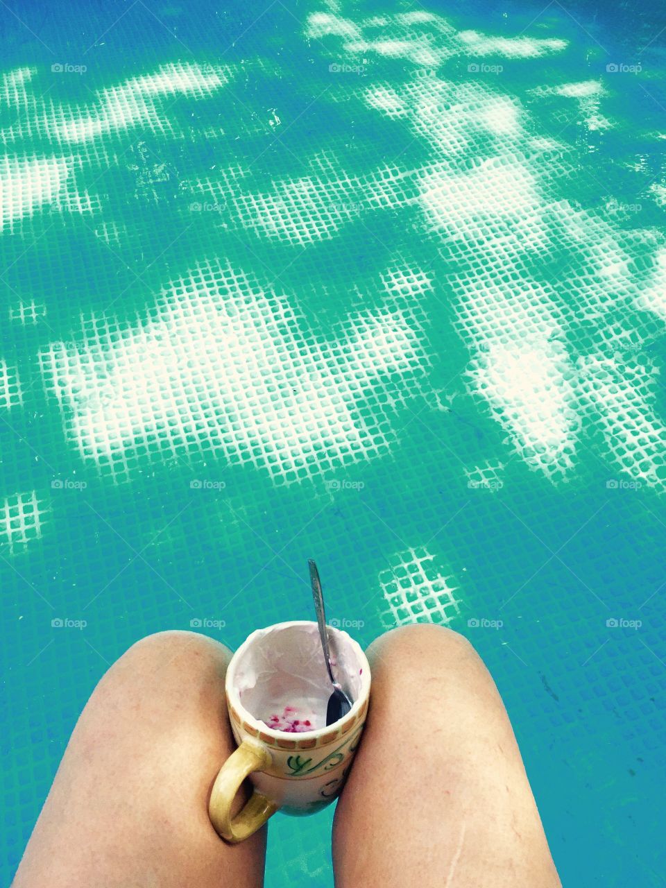 Legs in swimming pool with a cup between them and snack in cup.