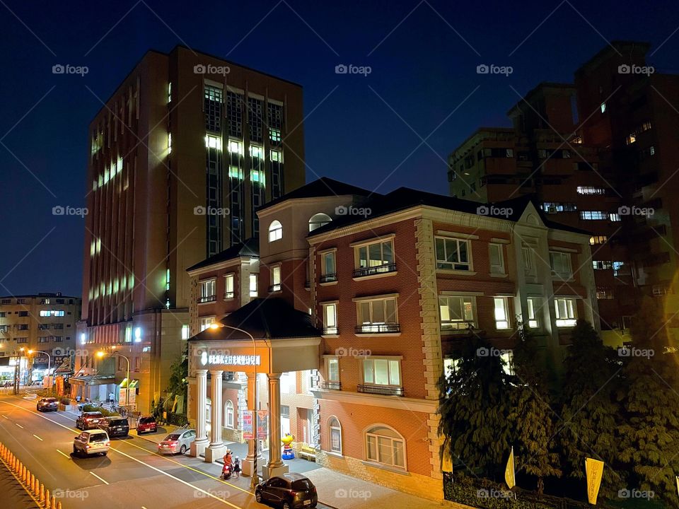 Several buildings against a deep blue night sky. The buildings are orange brick, and there are some trees. 