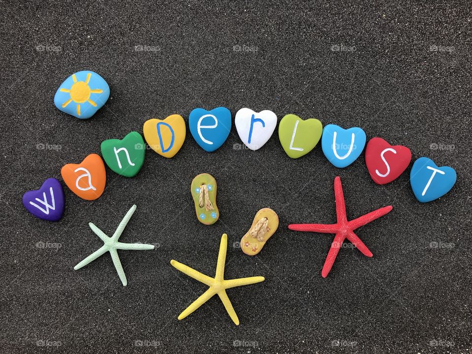 Wanderlust text composed with colored heart stones over black volcanic sand