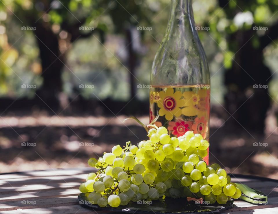 Grapes and homemade wine on a wooden table under dappled sunlight 