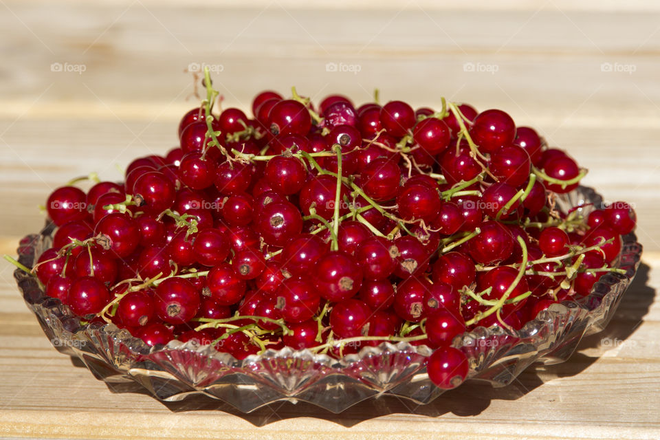 Red currant on glass dish placed on wood 