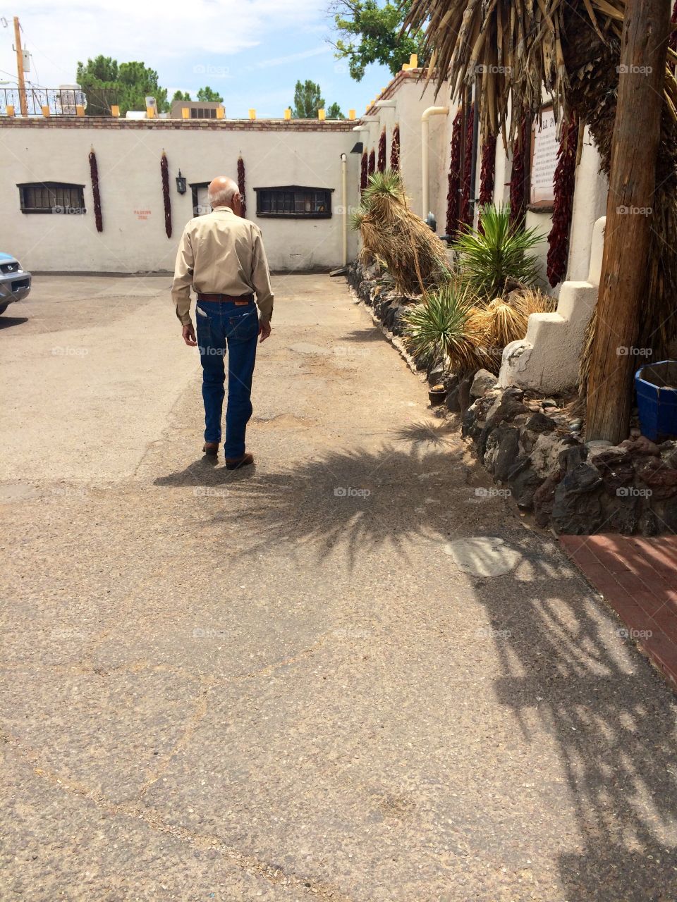 Old man walking in front of a southwestern style building 