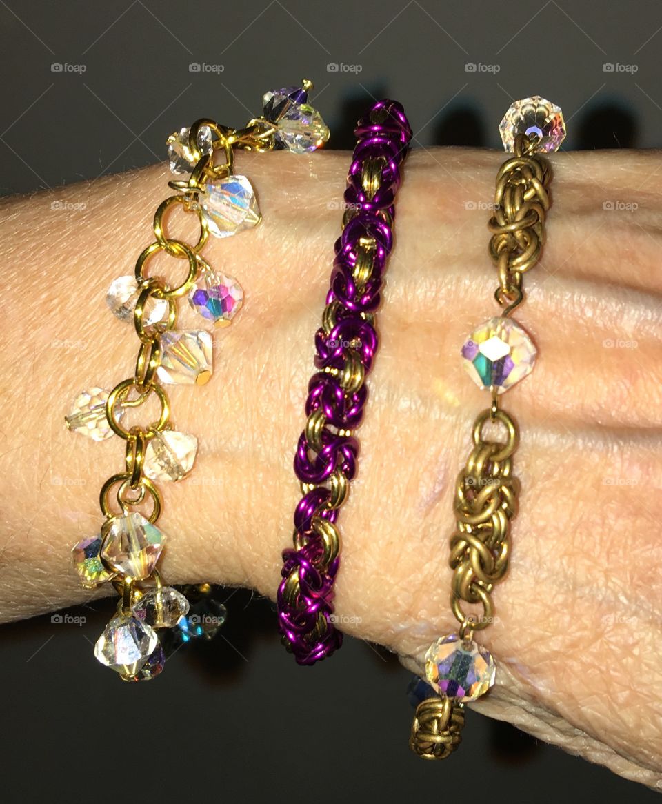 Three styles of handmade ladies bracelets! Crystals in two & the third of colored metal. The first crystal bracelet has each crystal hanging from a loop which helps it catch the light amazingly & sparkle as it moves. The second has the crystals made as part of the bracelet itself, catching the light as you move your arm. The third is a simpler style made of purple & gold color loops!