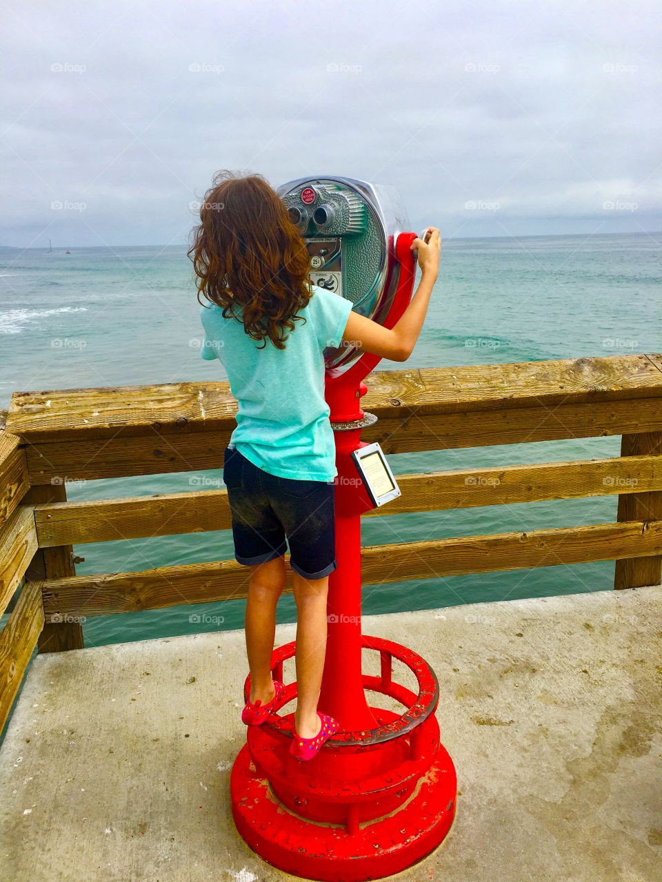 Little girl looking at ocean through coin-operated binoculars