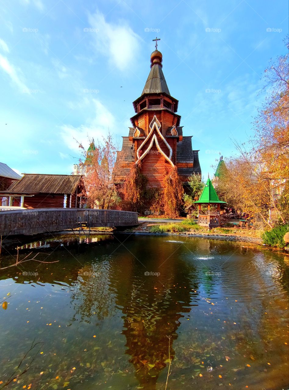 Autumn.  A pond that reflects: yellow birches, a wooden church, a wooden gazebo, a wooden bridge