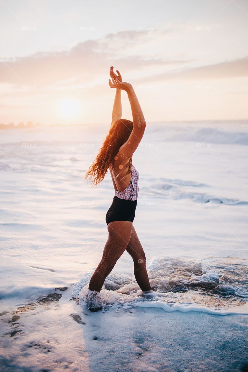 Girl plays in the foam as waves crash and the sun sets.