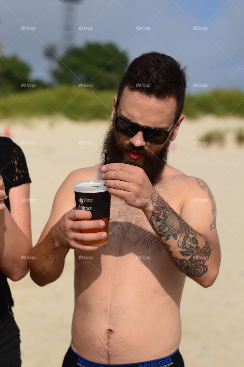 man with tattoos engoying beer on the beach on hot summer day