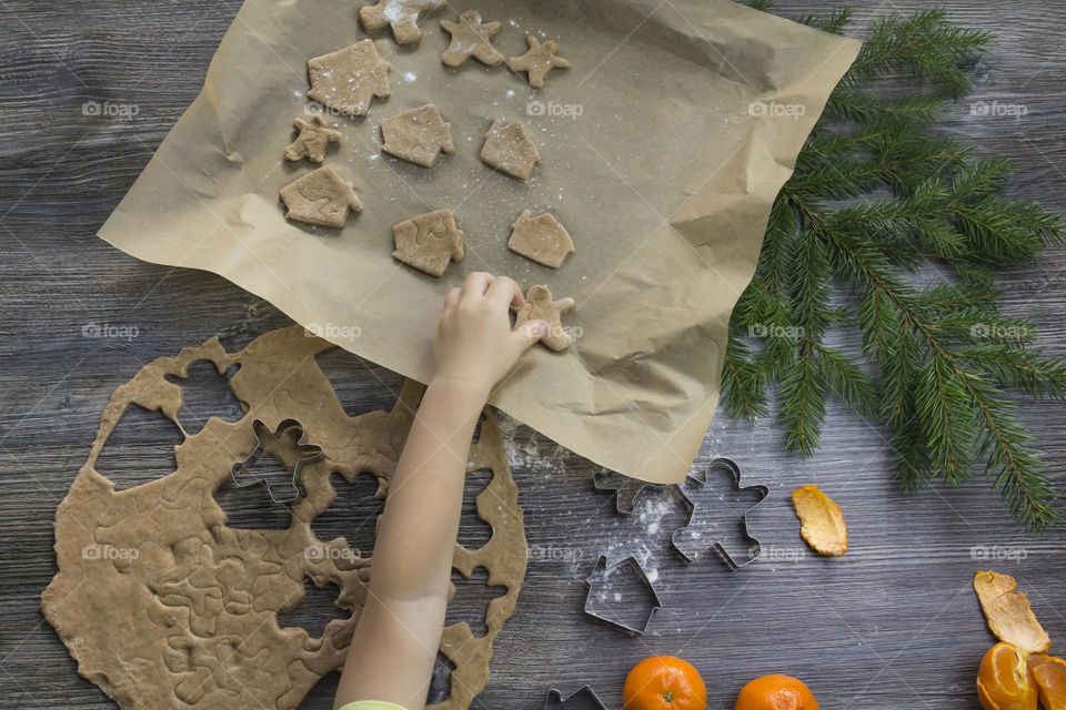 A small child helps to prepare festive, gingerbread cookies on a wooden table on Christmas Eve.