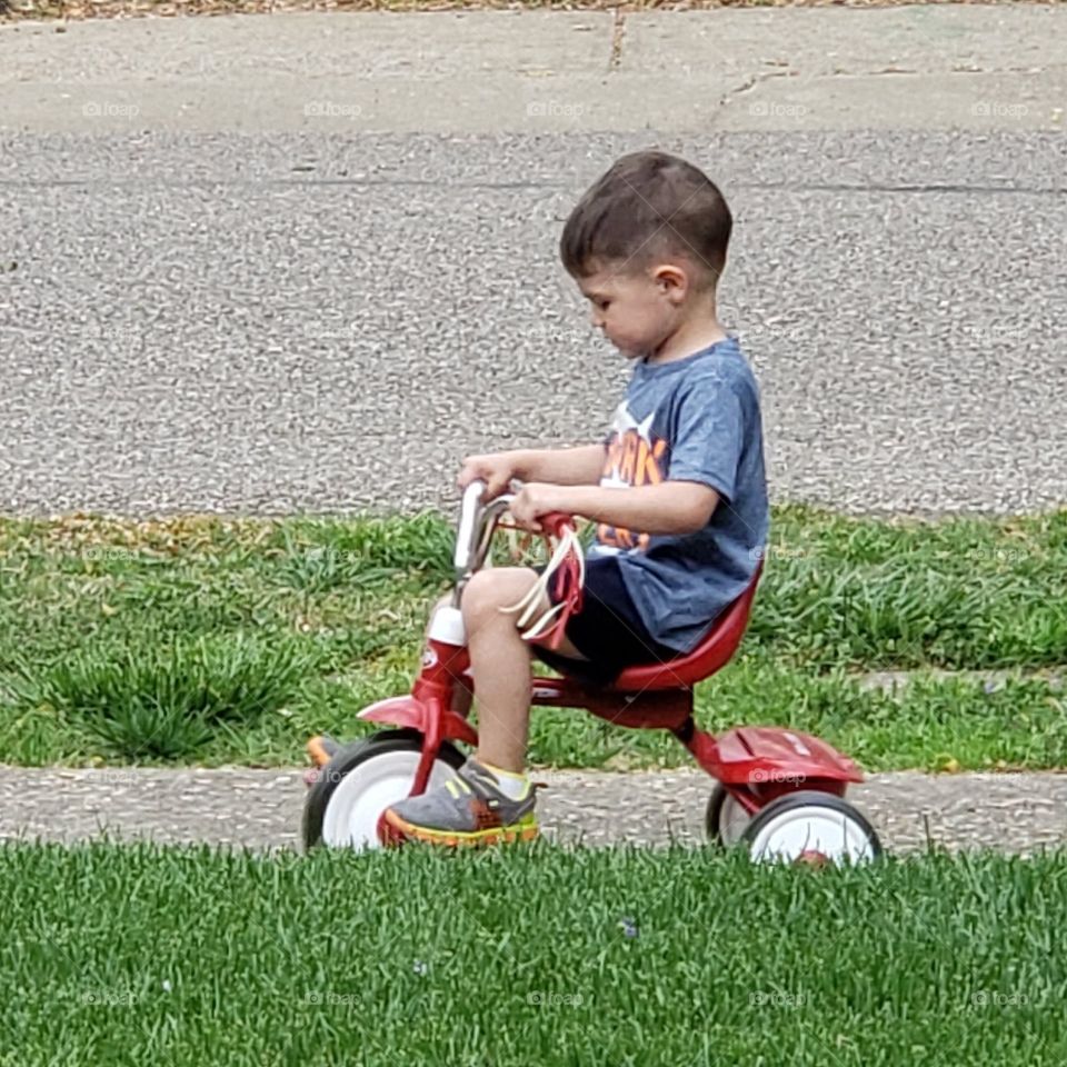 A child with full focus an a bundle of determination to get that trike down that sidewalk by himself