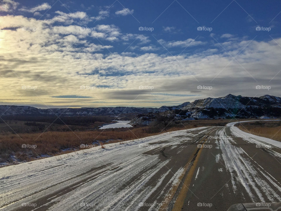 A partially snow-covered road through Theodore Roosevelt National Park in North Dakota near sunset.