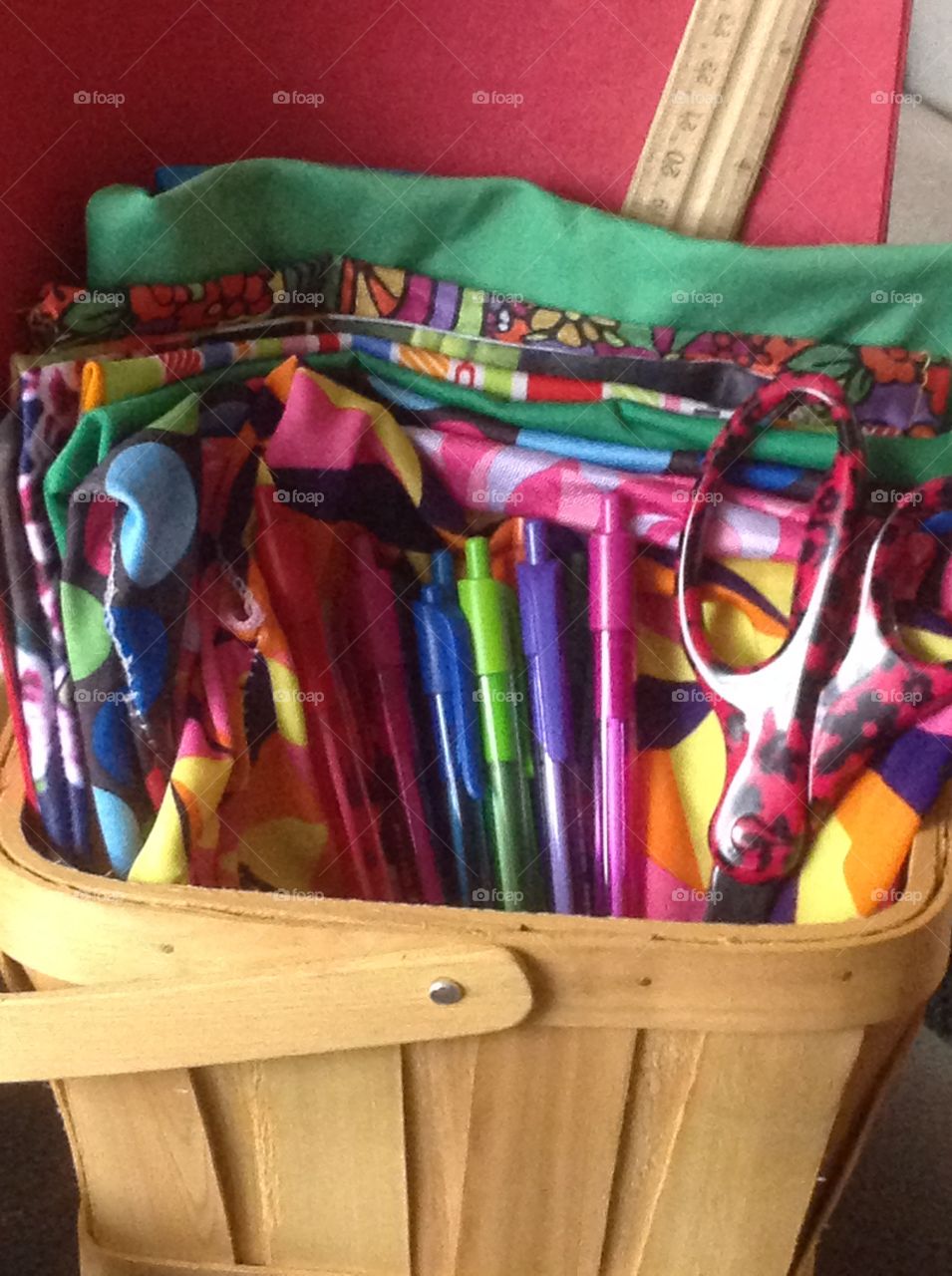 Fabrics, pens and scissors on a basket for art supplies.