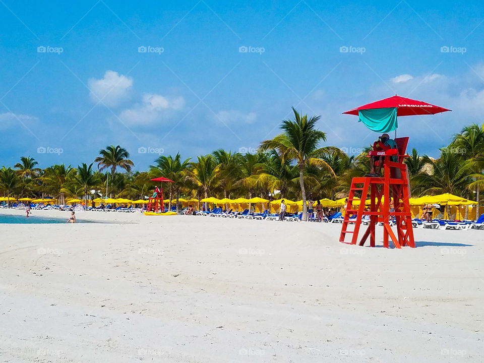 Sunny yellow umbrellas and bright red lifeguard chairs on the beach in Belize