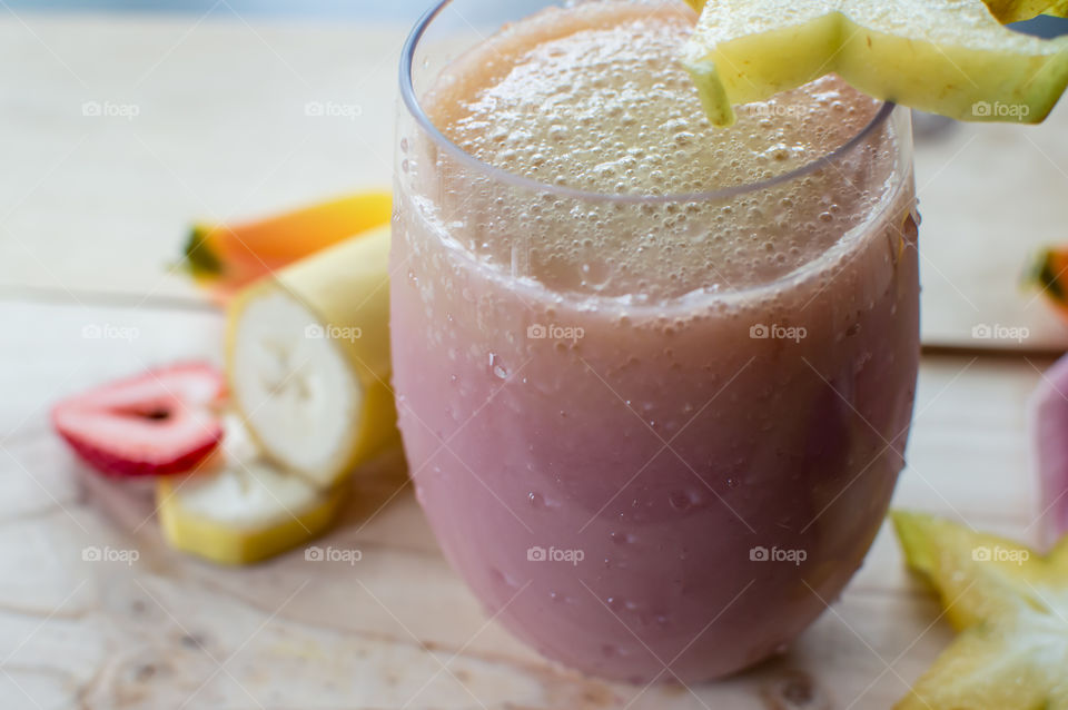 Beautiful fresh pink and white smoothie in glass with fresh strawberry heart and banana in background 