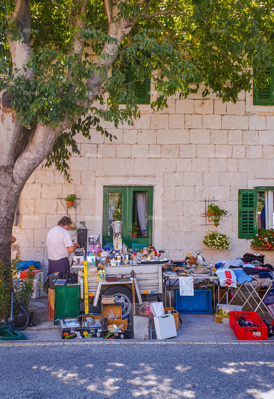 Croatia, Dalmatia, Brela. Weekly summer fair. A street with a stone house and a counter with all kinds of household utensils. Sale of unnecessary things. The second life of old household items: toys, books, CDs.