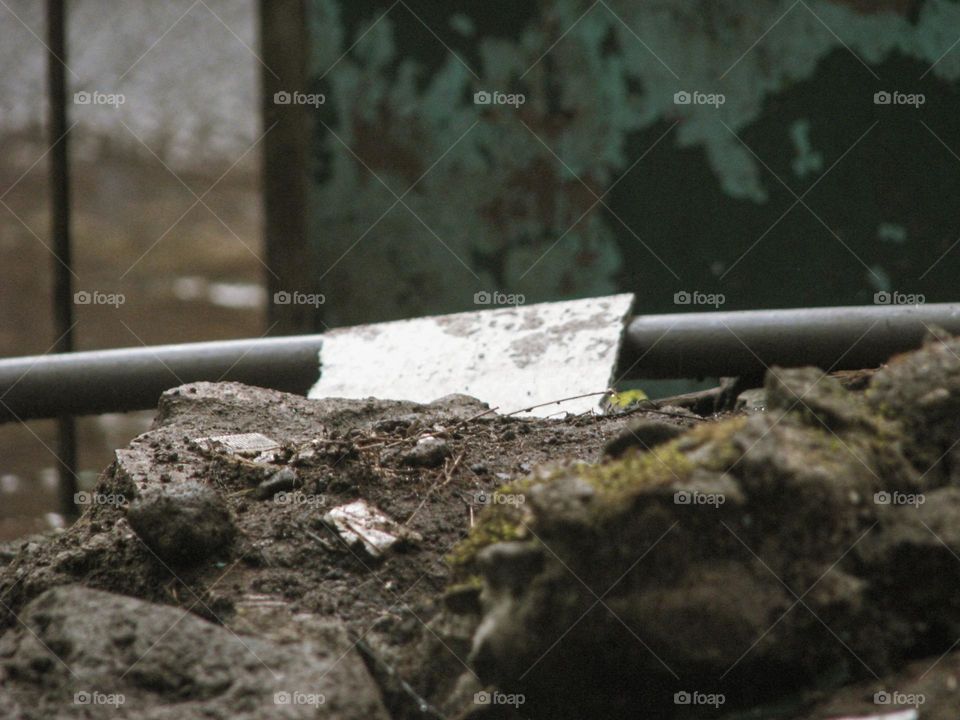 Close-up of a rough, uneven patch of ground with pieces of dirty white plasterboard lying on it, surrounded by a blurred background in low angle view