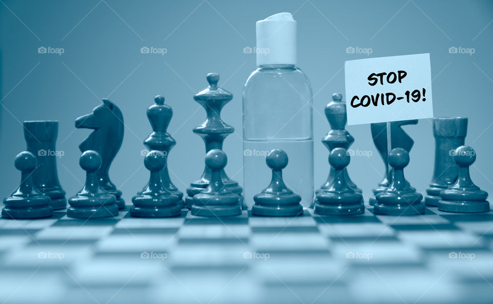 Coronavirus concept image chess pieces and hand sanitizer on chessboard illustrating global struggle against novel covid-19 outbreak.
