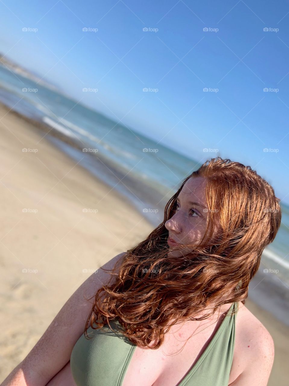Cute redheaded model with beachy waves standing on a beautiful empty beach on the coast