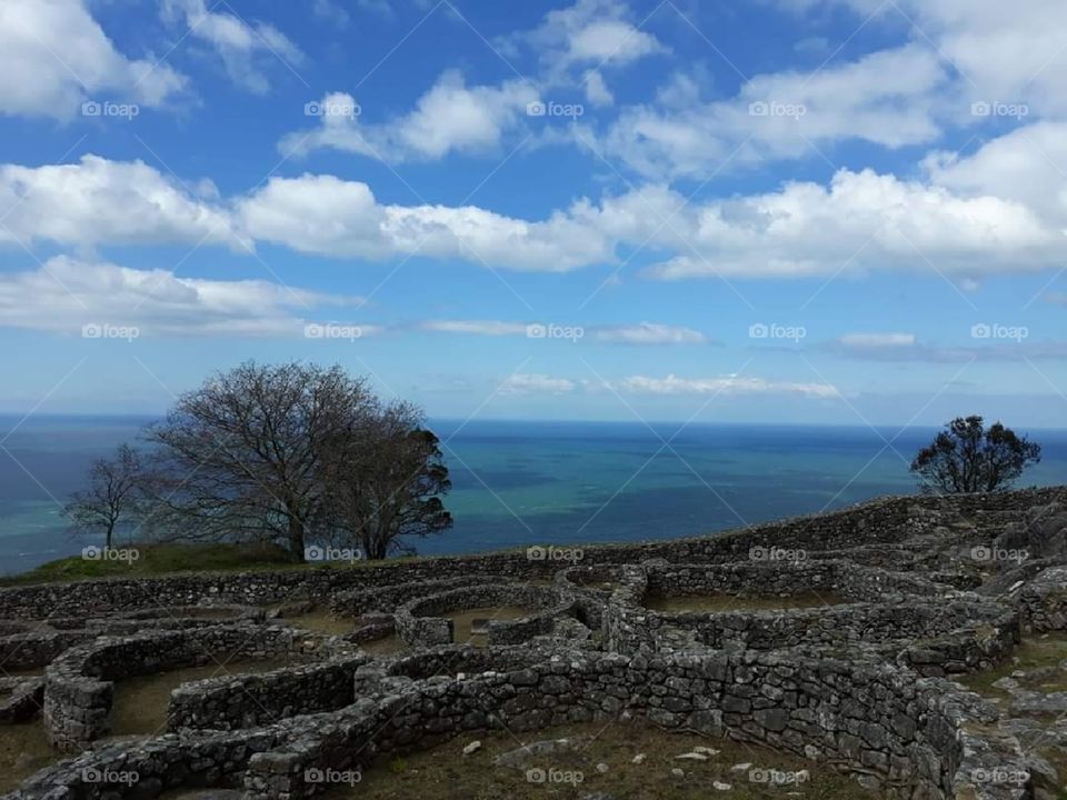 Un castro (archaeological ruins from an iron age settlement) on a hillside overlooking the beautiful blue and green sea. Clouds and a tree are present.
One of the most peaceful places I have ever been to.❤