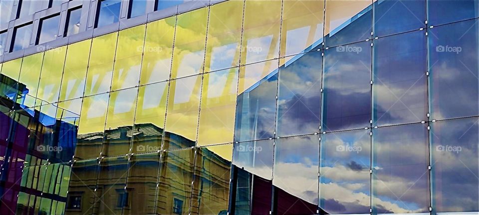 This ultramodern building in the inner city of “Munich”, capitol of “Bavaria” reflects all of its surroundings: the neighboring houses and the plentiful cumulus clouds in the bright blue sky. 2024. Hypnotic Productions