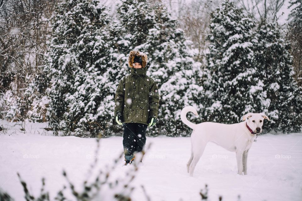 Young boy standing in the snow with his dog