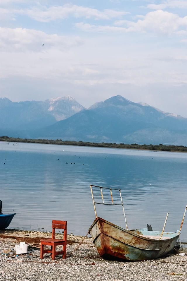 rusty boat and red chair on the border of the lake with mountain in the background
