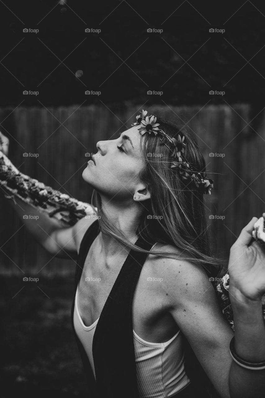 Black and white retro vibe image of a young woman wearing a crown of flowers and feeling the blowing wind with her eyes closed 