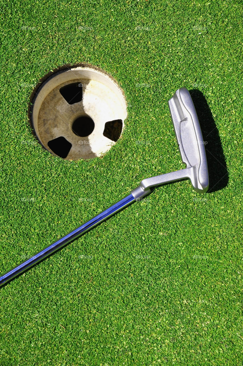 Golfing concept.  Golf putter lying on green by hole.