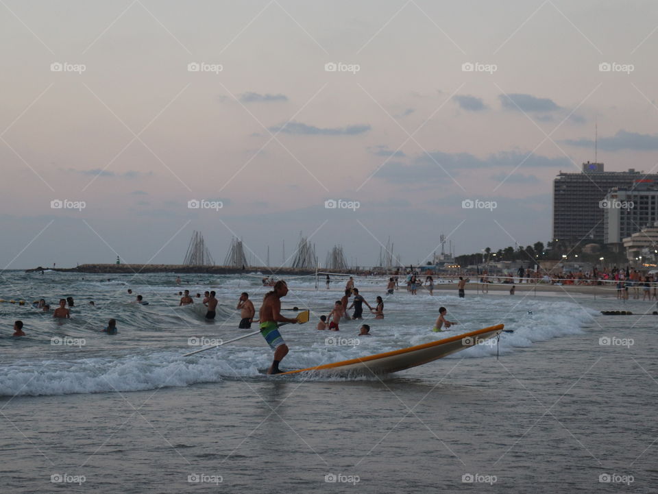 Grey sky and beach with people and a surfboard 