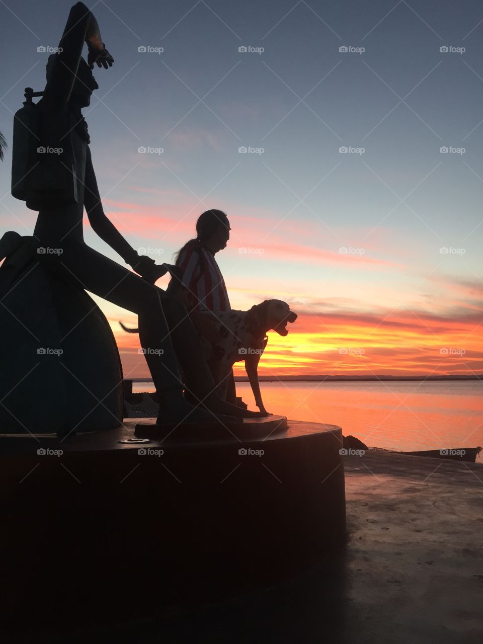Man and dog silhouetted at sunset at statue on the malecon (sidewalk along the bay)