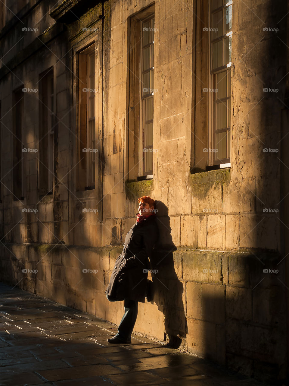 Woman leaning against masonry building and sunbathing in autumn warm evening sun.