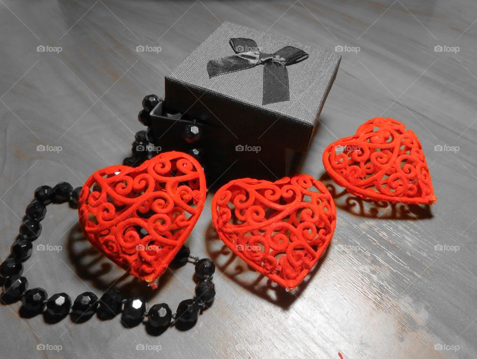 Три красных сердца, чёрная коробочка с подарком, чёрные бусы из камня агат. Всё это располагается на столе.