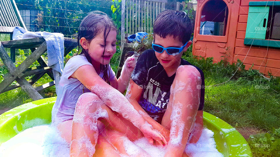 My children playing in the garden with water and soap  in the summer
