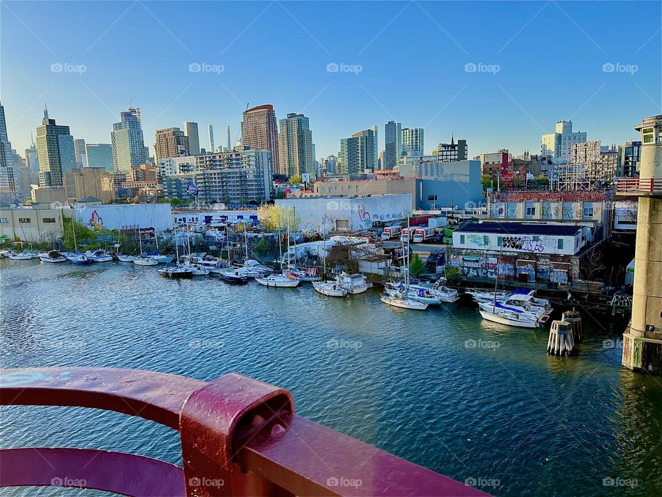 This is the view from the “Pulaski Bridge” that connects “Greenpoint”, Bklyn and LIC, Queens overlooking “Newtown Creek” with its many boats in the warm light of the setting evening sun. In the distance we see “Manhattan”. 2024. Hypnotic Productions
