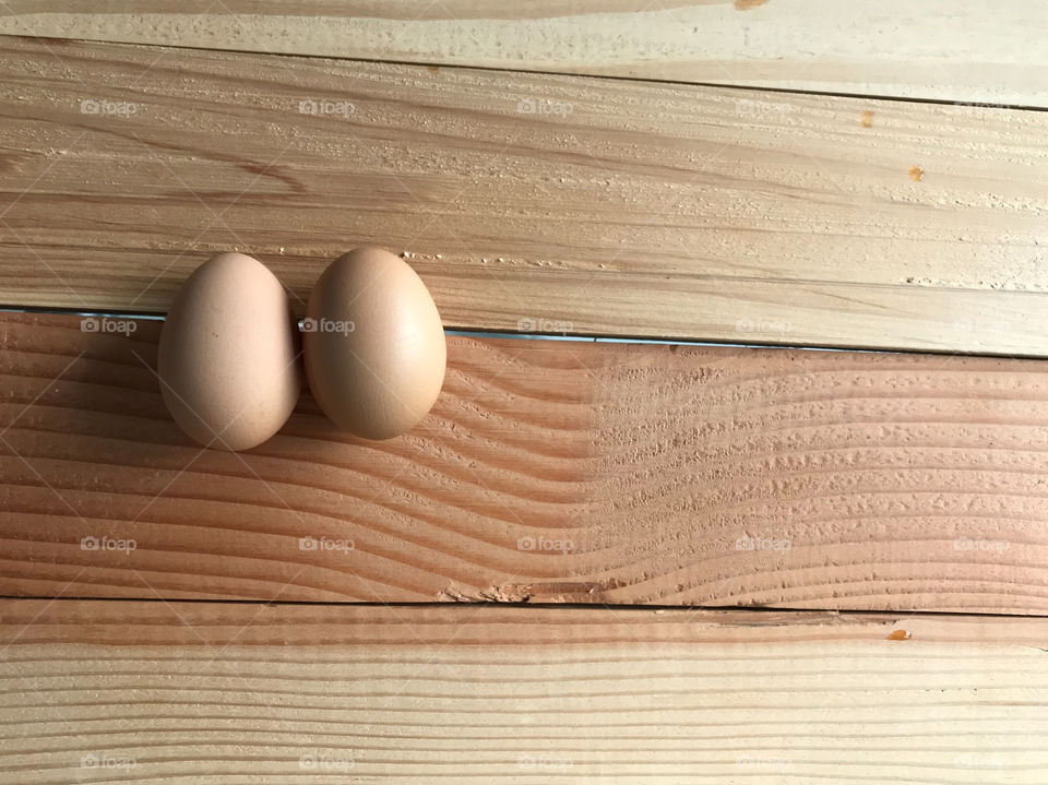 two fresh chicken eggs on natural rubber wood board with copy space on right side of frame