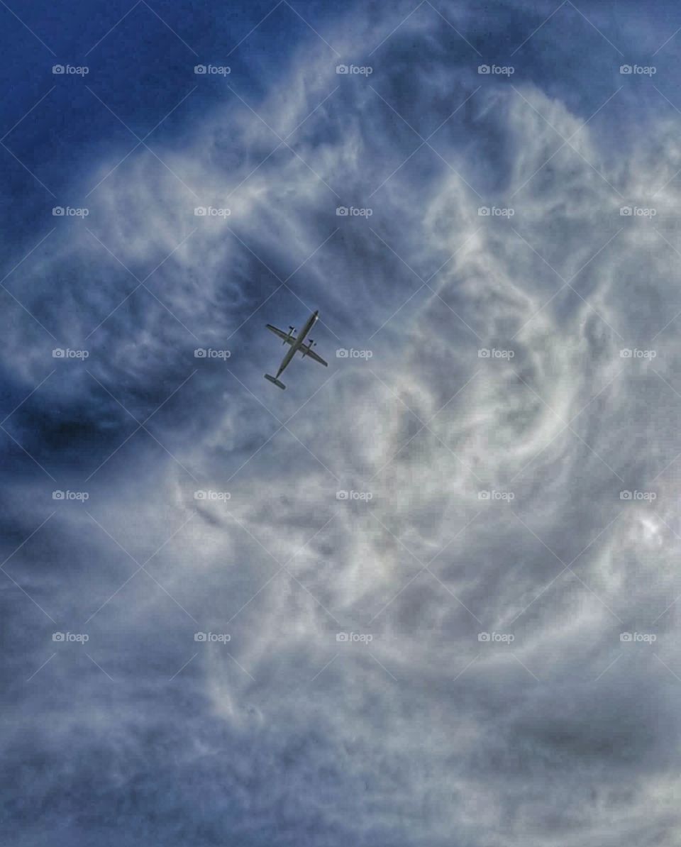 An head view of an airplane fling overhead with cool clouds in a blue sky